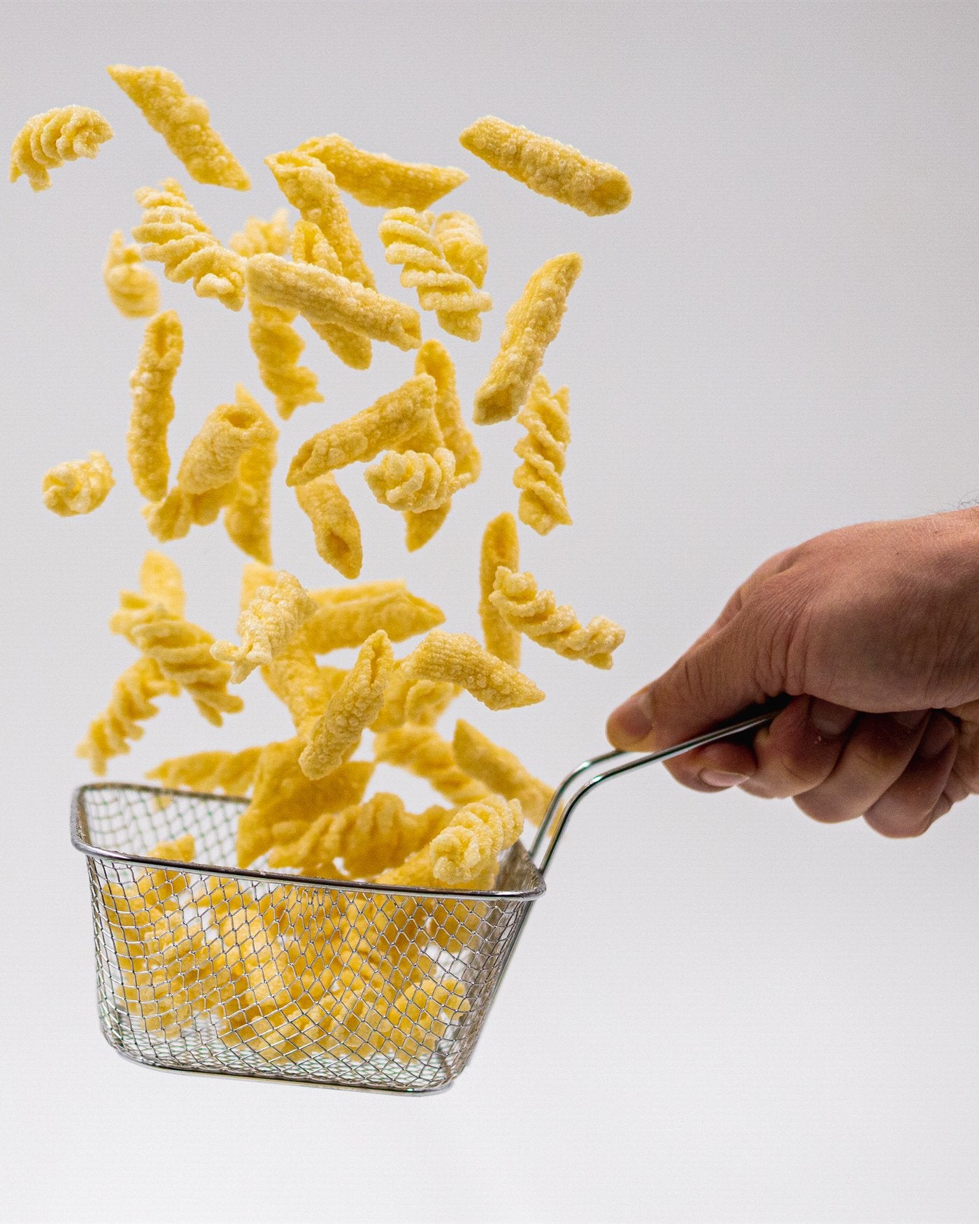 Pasta chips falder ned i en frituresi, holdt i hånden